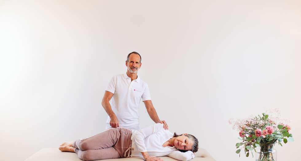Osteopressur Mann behandelt eine Frau, die seitlich auf einer Liege liegt.
